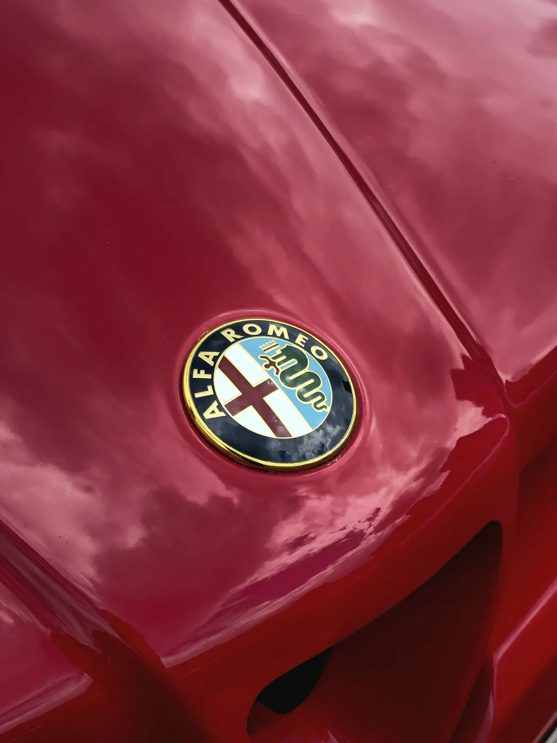 Badge Alfa Romeo sur un capot rouge : croix de Milan à gauche, Biscione à droite